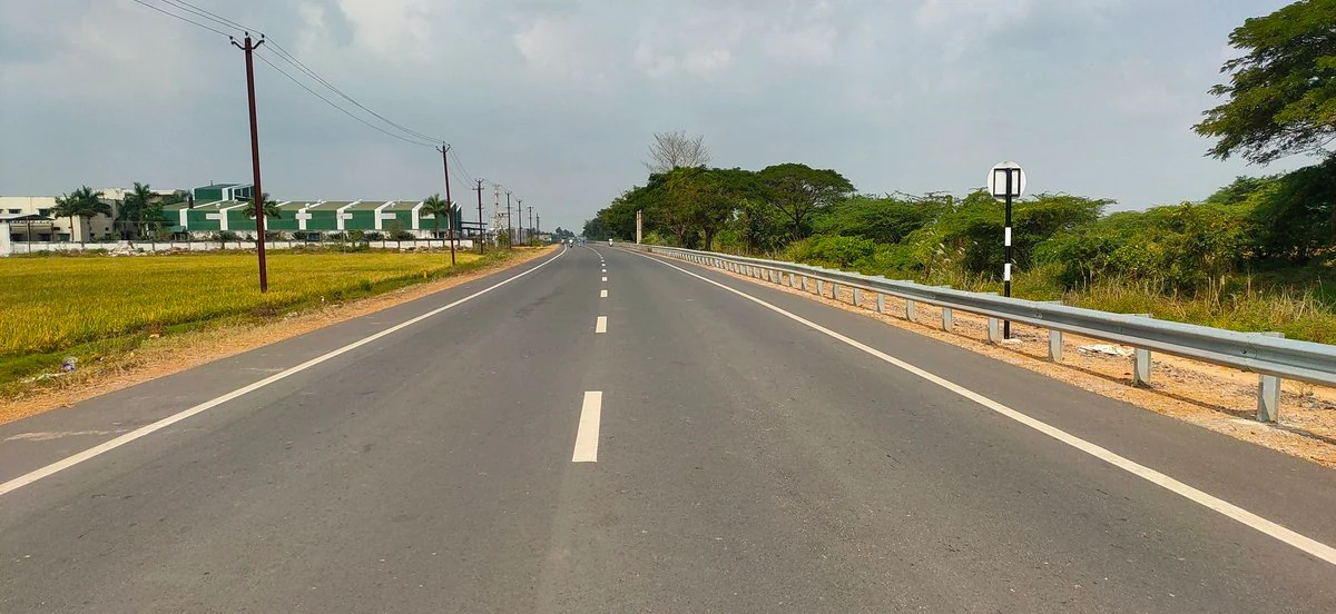 A completed highway with lane markings and roadside barriers between Kumbakonam and Mannargudi.