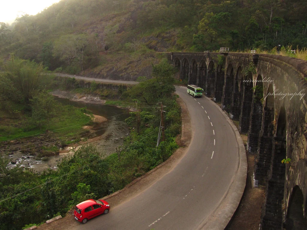A road bends beside a historic masonry railway viaduct on the Shenkotta–Punalur corridor.